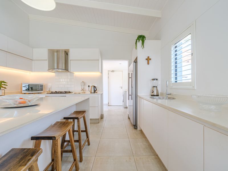 Modern, well-maintained kitchen featuring sleek white cabinetry, stone countertops, integrated gas hob, extractor fan, and tiled flooring with ample natural light.