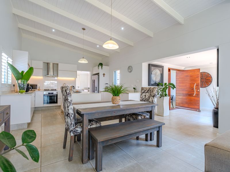 Spacious open-plan kitchen and dining area featuring vaulted ceilings with exposed beams, modern cabinetry, stone countertops, and tiled flooring throughout.