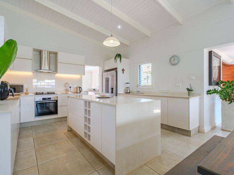 Modern, bright kitchen featuring a central island, quartz countertops, subway tile backsplash, built-in appliances, and a high vaulted ceiling with clean finishes.