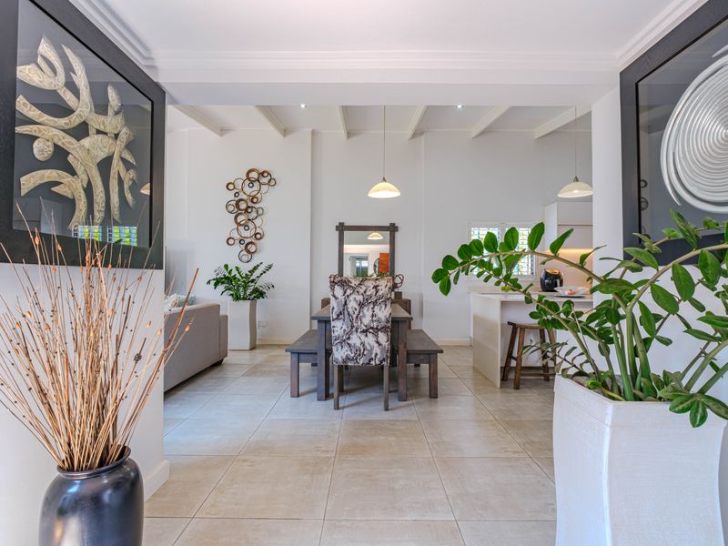 An open-plan living and dining area featuring tiled flooring, exposed ceiling beams, and a modern kitchen island with integrated cabinetry.