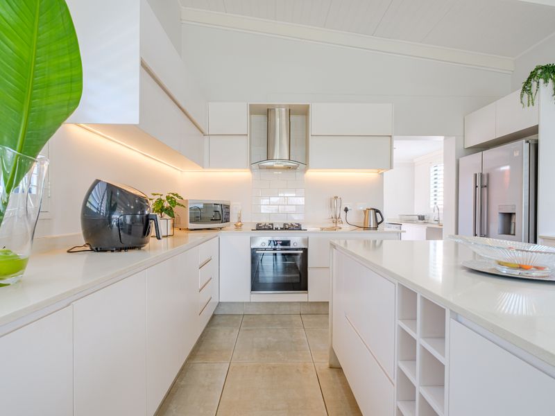 Modern, well-lit kitchen featuring sleek white cabinetry, stone countertops, a central island, and high-quality built-in appliances with a clean subway tile backsplash.