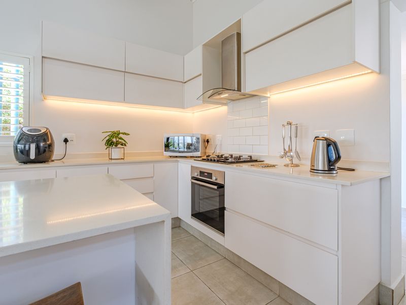 Modern kitchen featuring sleek white cabinetry, stone countertops, integrated gas hob, built-in oven, extractor fan, and stylish under-cabinet lighting.