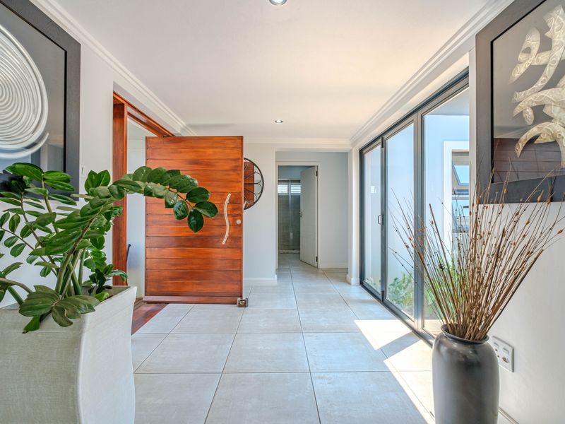 Bright and modern entrance hall featuring a large timber pivot door, large format floor tiles, and expansive glass sliding doors leading to the exterior.