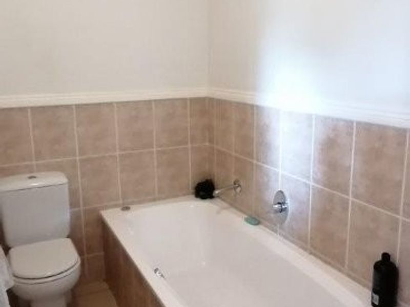 A functional bathroom featuring a built-in bathtub with tiled surround, ceramic wall and floor tiling, and a standard toilet.