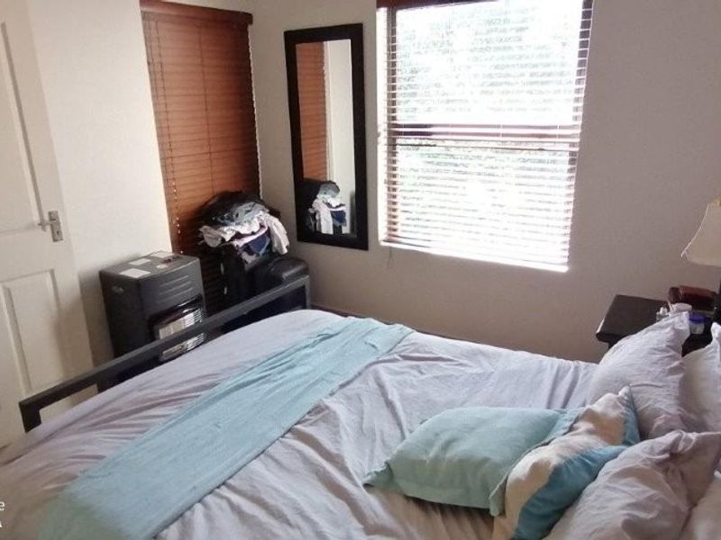 A standard bedroom featuring a window with venetian blinds and a neutral interior finish.