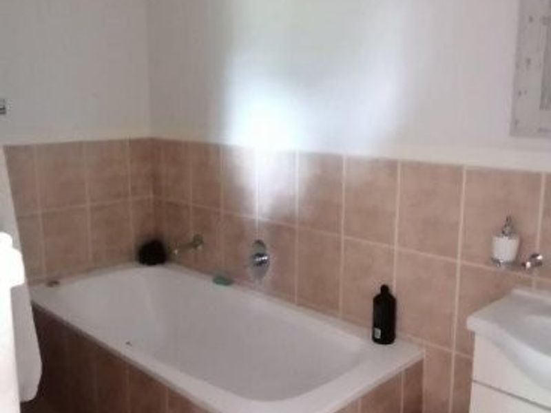 A functional bathroom featuring a built-in bathtub with tiled surround, a vanity cabinet, and neutral ceramic floor tiling.