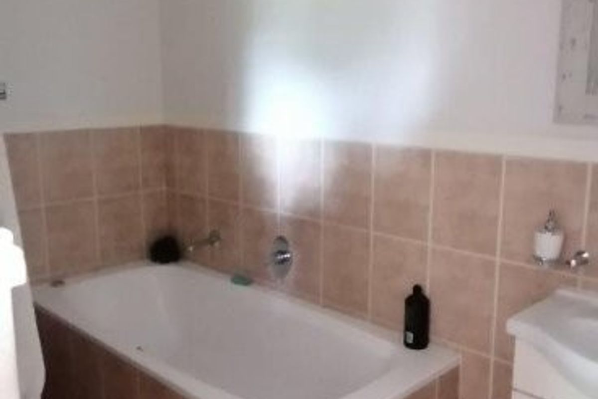 A functional bathroom featuring a built-in bathtub with tiled surround, a vanity cabinet, and neutral ceramic floor tiling.