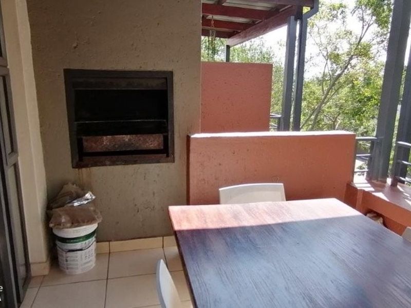 Covered balcony featuring a built-in braai, tiled flooring, and metal railings, offering an outdoor entertainment space.