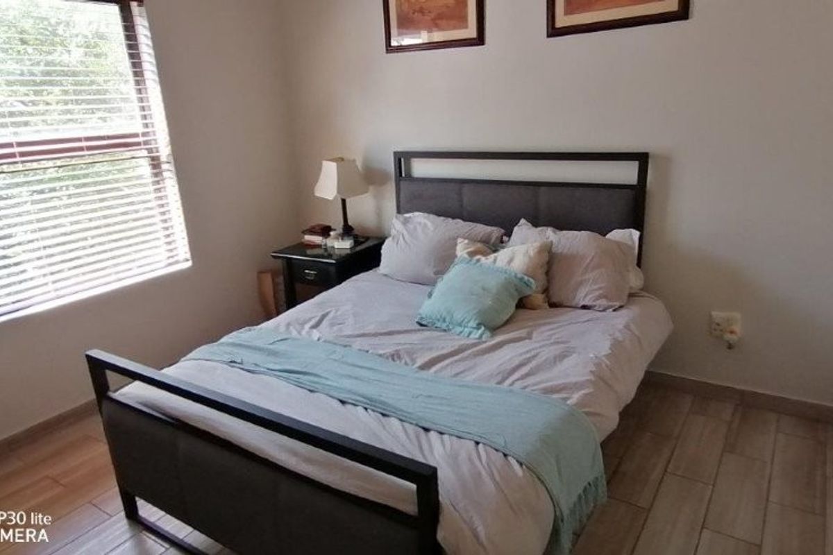 A functional bedroom featuring tiled flooring, a window with venetian blinds, and built-in wardrobe storage.