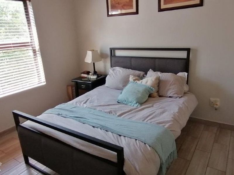 A functional bedroom featuring tiled flooring, a window with venetian blinds, and built-in wardrobe storage.