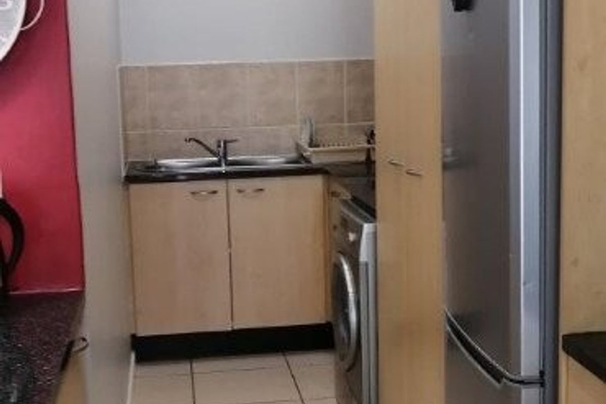 A functional scullery area featuring built-in cabinetry, a stainless steel sink, tiled splashback, and tiled flooring, providing efficient utility space.