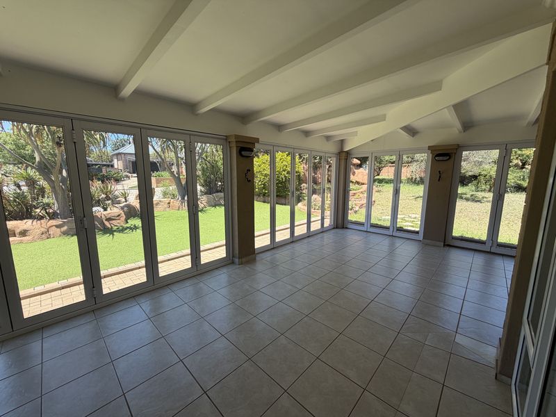 Spacious covered patio featuring tiled flooring, exposed beam ceiling, and extensive bi-fold glass doors providing seamless access to the garden.