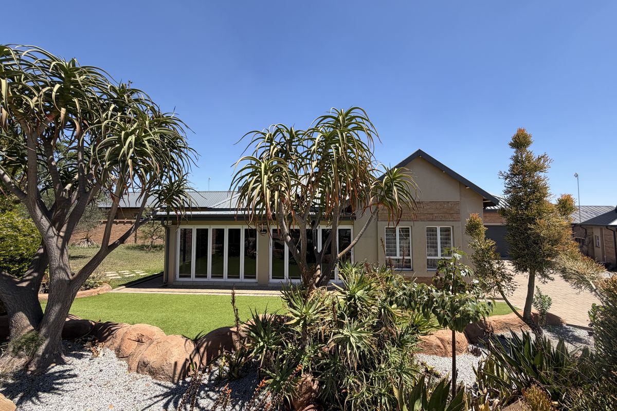 A well-maintained rear exterior view of the house featuring bi-fold doors, a metal roof, and a landscaped garden with artificial lawn.