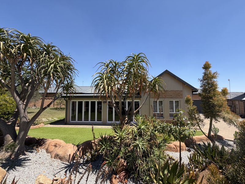 A well-maintained rear exterior view of the house featuring bi-fold doors, a metal roof, and a landscaped garden with artificial lawn.