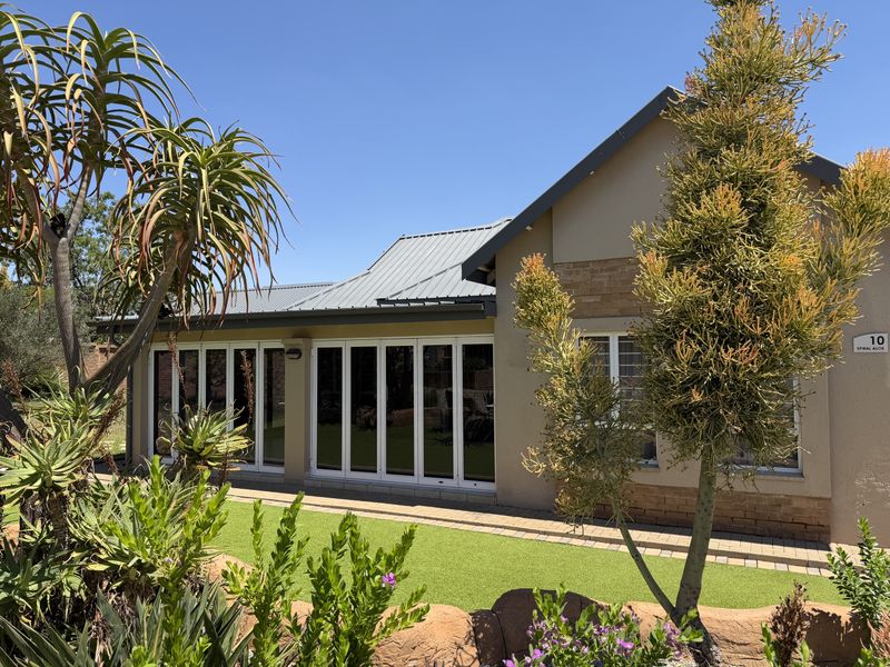 Rear view of the property featuring a metal roof, white bi-fold doors opening to a paved walkway, and a well-maintained artificial lawn garden.