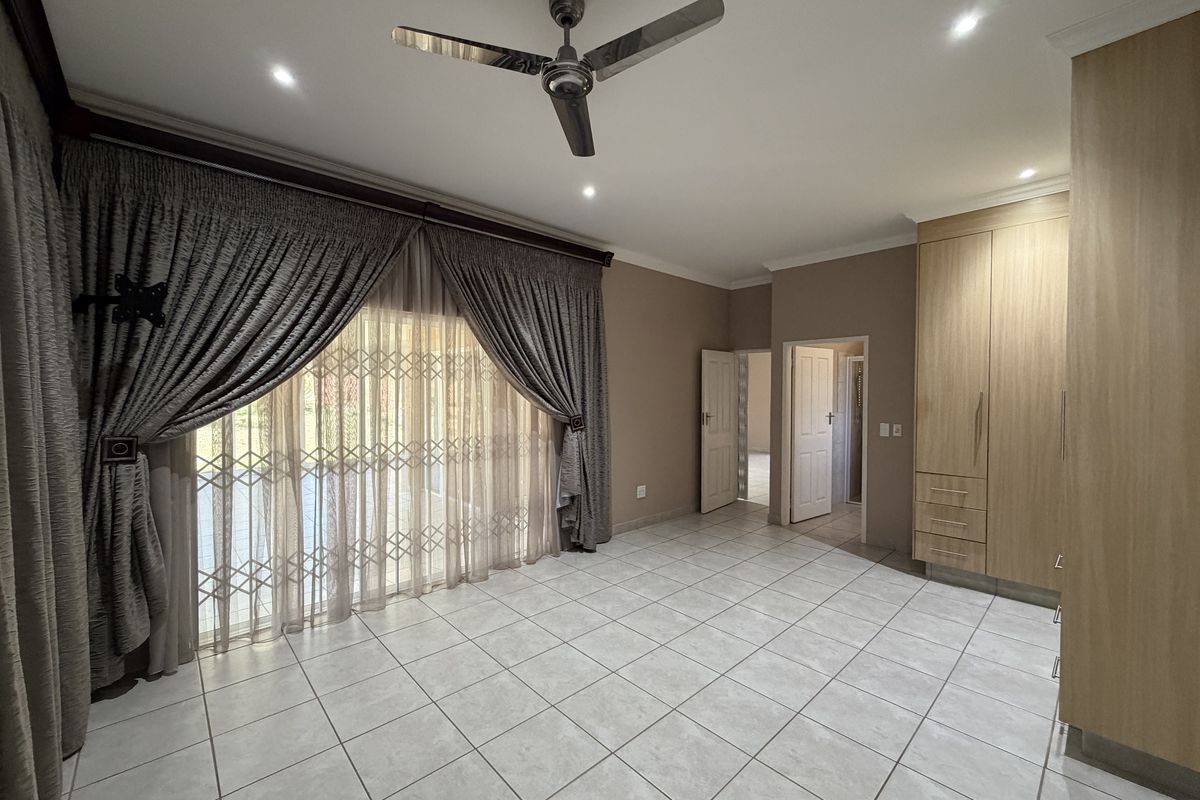 Spacious bedroom featuring tiled flooring, built-in cupboards, recessed lighting, a ceiling fan, and a sliding glass door with a security gate.