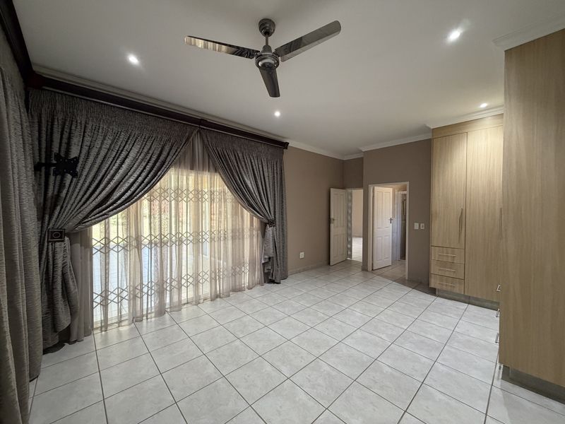 Spacious bedroom featuring tiled flooring, built-in cupboards, recessed lighting, a ceiling fan, and a sliding glass door with a security gate.