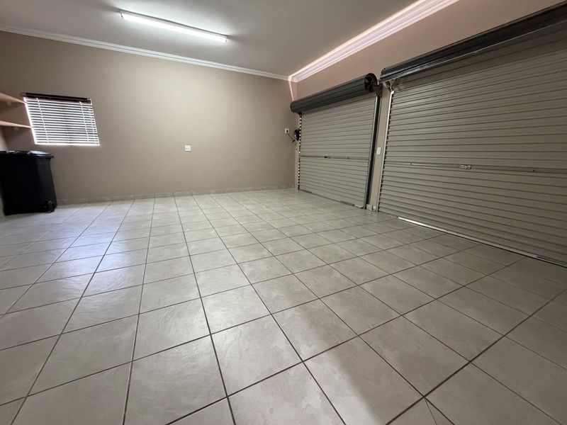 A spacious, well-maintained double garage featuring tiled flooring, roller shutter doors, and clean neutral wall finishes.