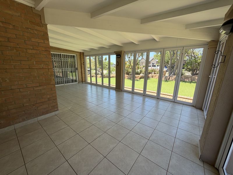 Spacious covered patio featuring tiled flooring, exposed beam ceiling, and large bi-fold glass doors opening onto the garden.