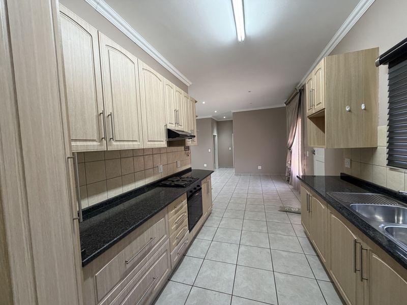 A functional kitchen featuring light wood cabinetry, dark granite countertops, built-in oven and hob, and tiled flooring in an open-plan layout.