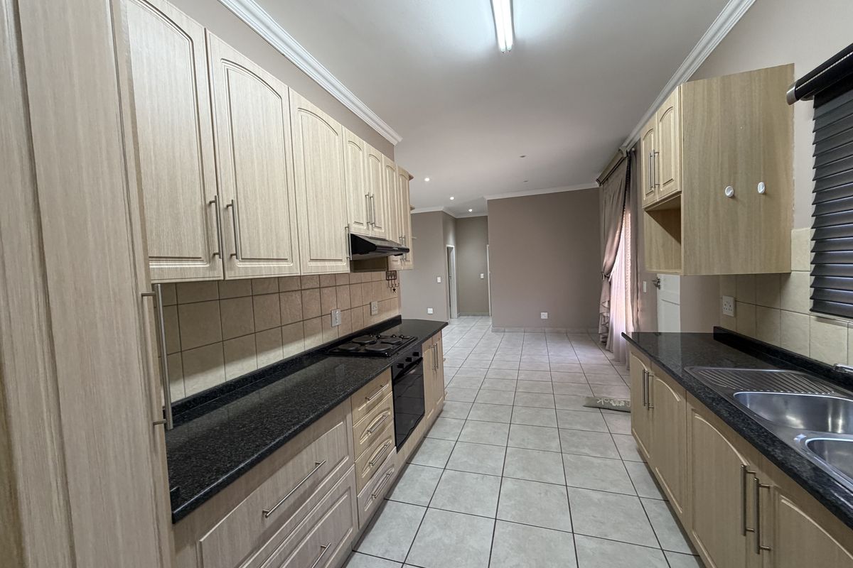 A functional kitchen featuring light wood cabinetry, dark granite countertops, built-in oven and hob, and tiled flooring in an open-plan layout.