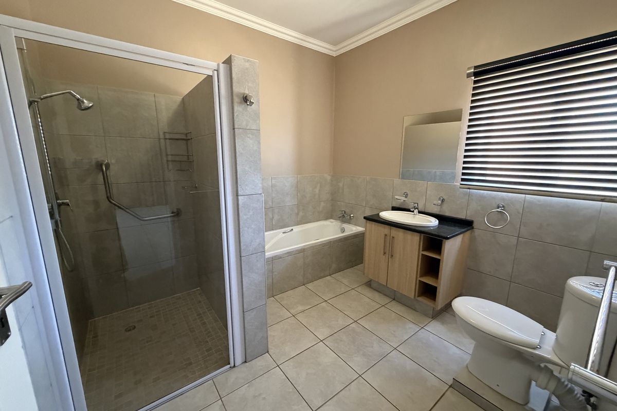 A clean and functional bathroom featuring a walk-in shower, built-in bathtub, vanity with basin, and toilet, finished with neutral wall and floor tiles.