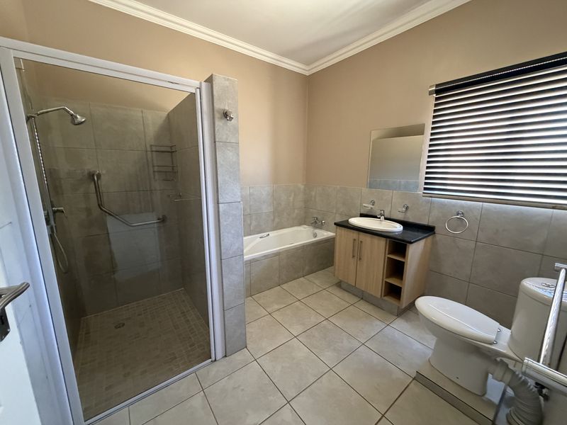 A clean and functional bathroom featuring a walk-in shower, built-in bathtub, vanity with basin, and toilet, finished with neutral wall and floor tiles.