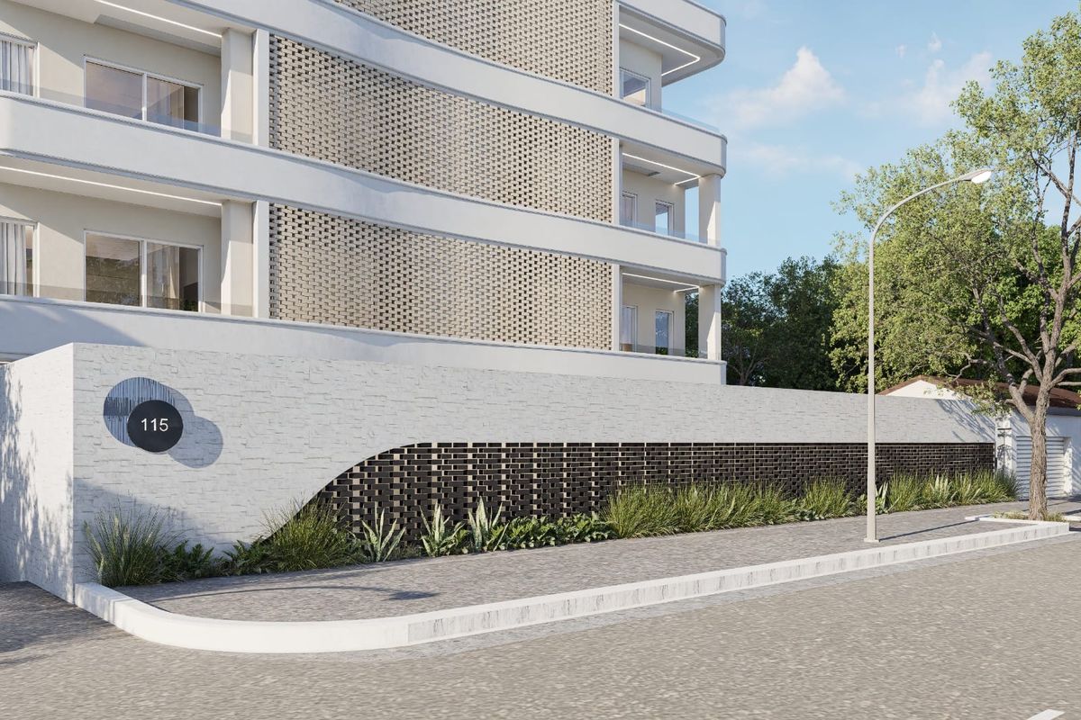 Modern apartment building exterior featuring a decorative brick boundary wall, paved sidewalk, and contemporary architectural design with glass-fronted balconies.