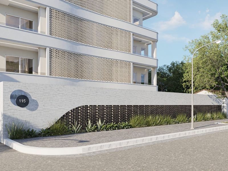 Modern apartment building exterior featuring a decorative brick boundary wall, paved sidewalk, and contemporary architectural design with glass-fronted balconies.
