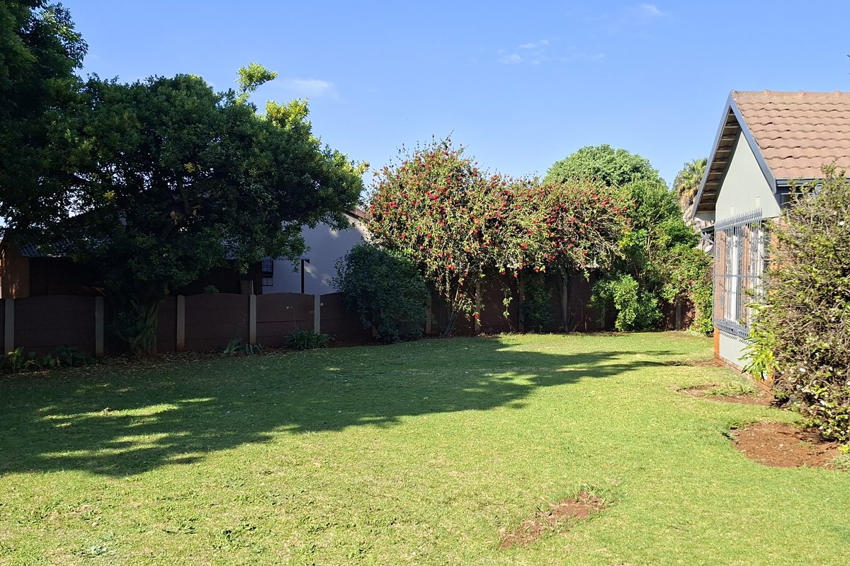 A spacious rear garden featuring a well-maintained lawn, mature trees, and a boundary wall, adjacent to the home's covered patio area.