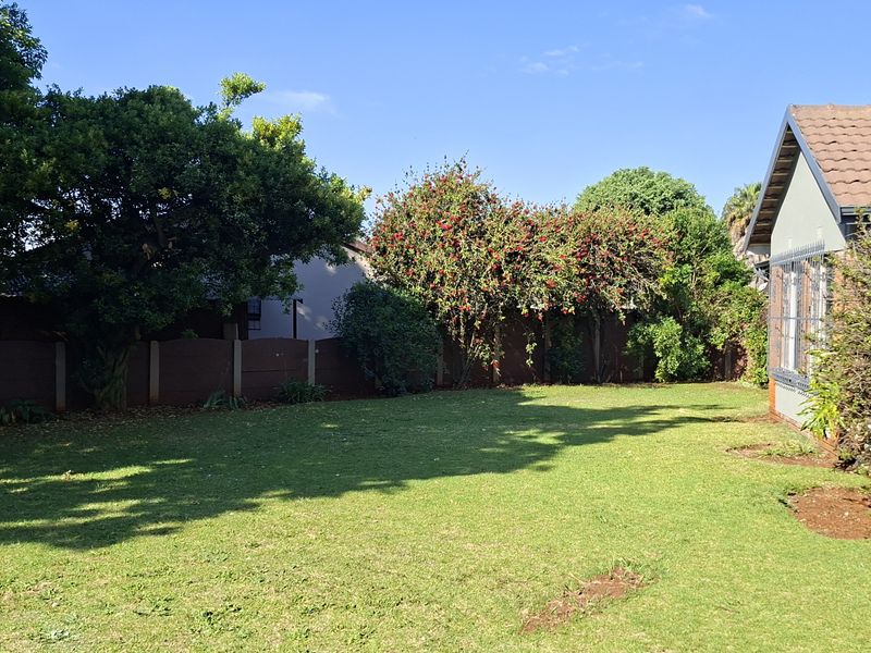 A spacious rear garden featuring a well-maintained lawn, mature trees, and a boundary wall, adjacent to the home's covered patio area.
