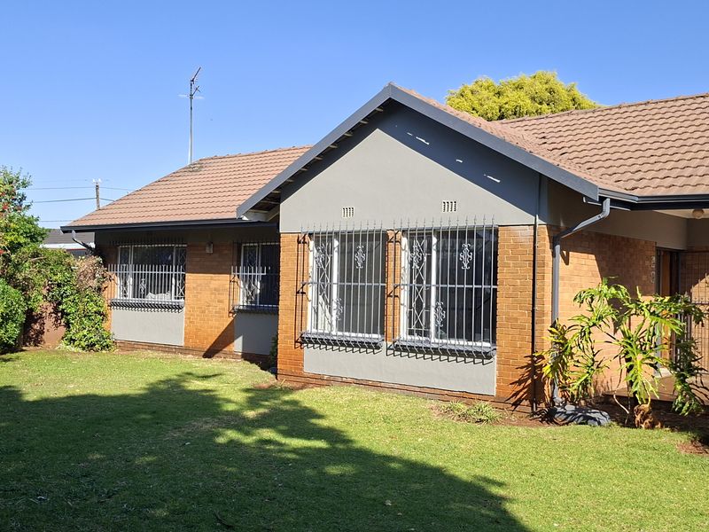 Rear view of a well-maintained facebrick house featuring a tiled roof, security bars on windows, and a spacious private garden.