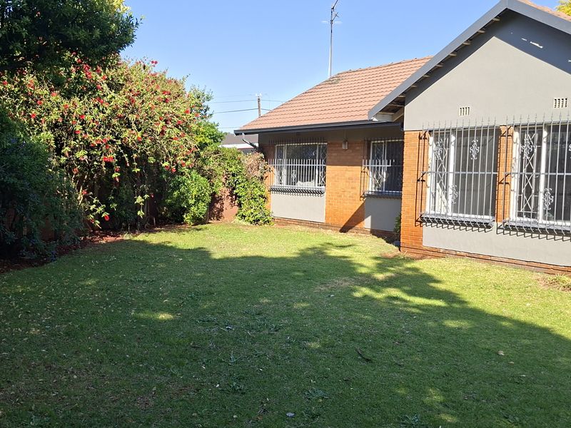 A view of the rear garden featuring a brick exterior, tiled roof, and secure window bars, set against a well-maintained lawn.
