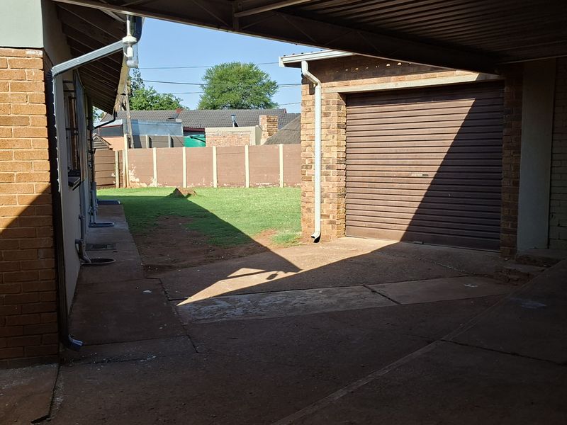 Rear exterior view featuring a paved driveway, carport structure, roller garage door, and access to the backyard area with boundary walling.