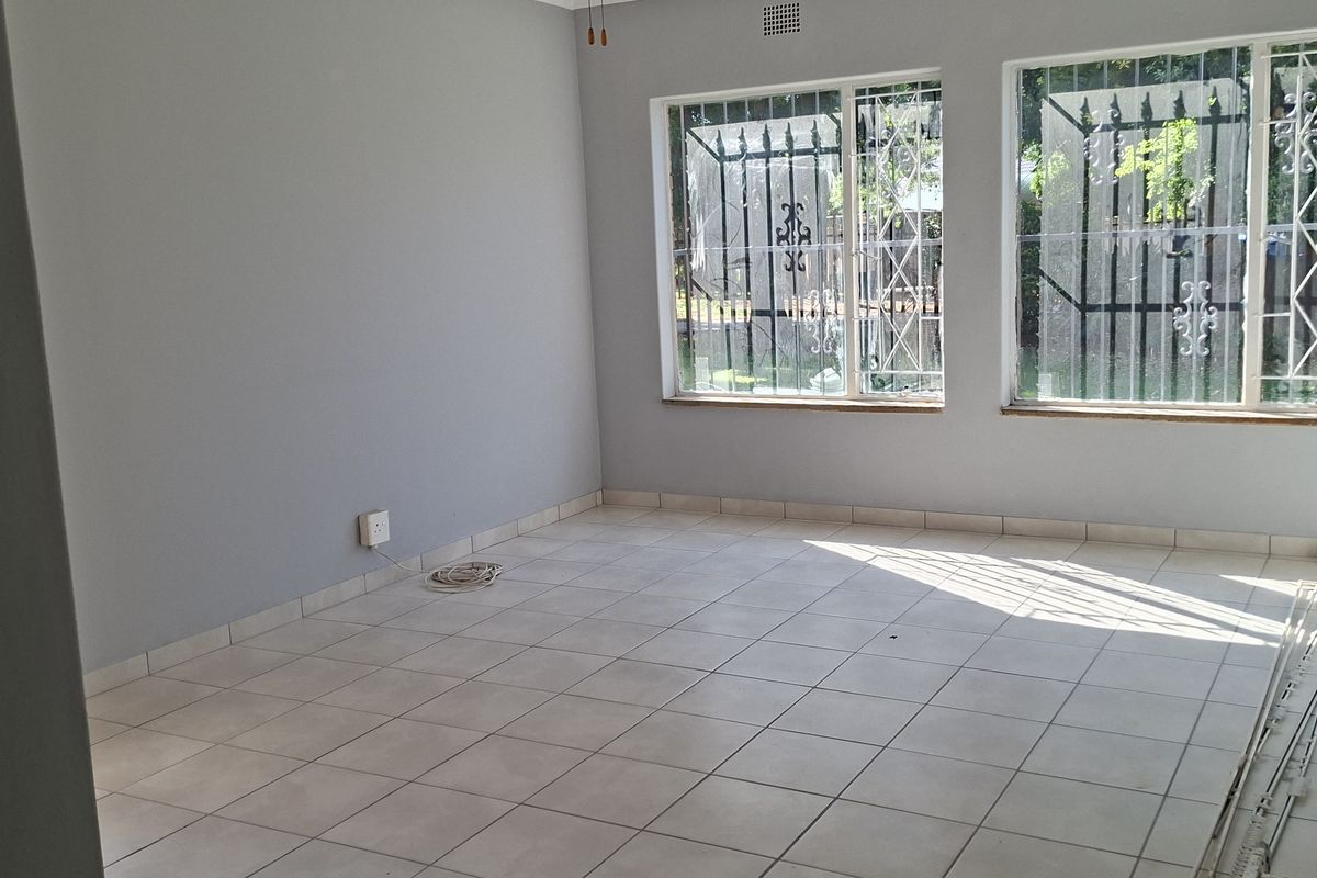An empty living room featuring neutral grey walls, tiled flooring, and windows fitted with security bars.