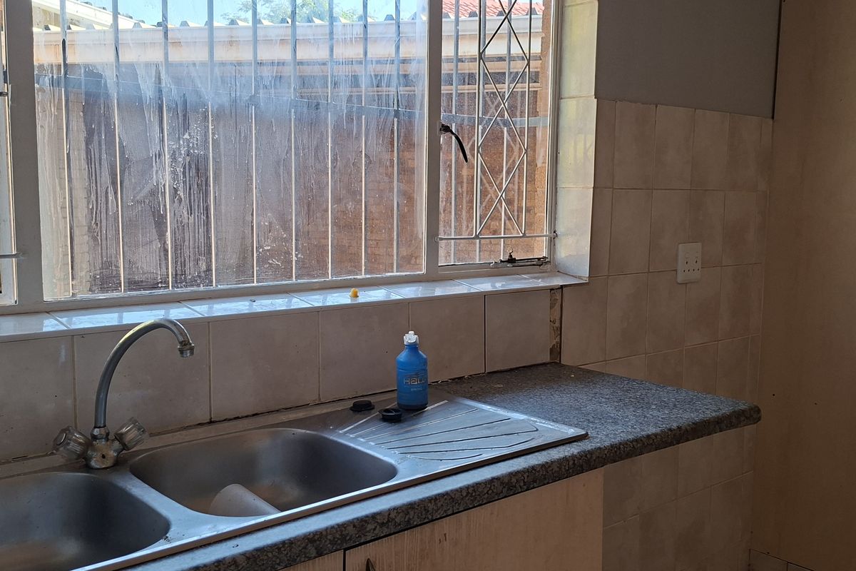 A functional kitchen area featuring a double bowl stainless steel sink, tiled splashback, and laminate countertops, requiring cosmetic updates to improve its overall condition.
