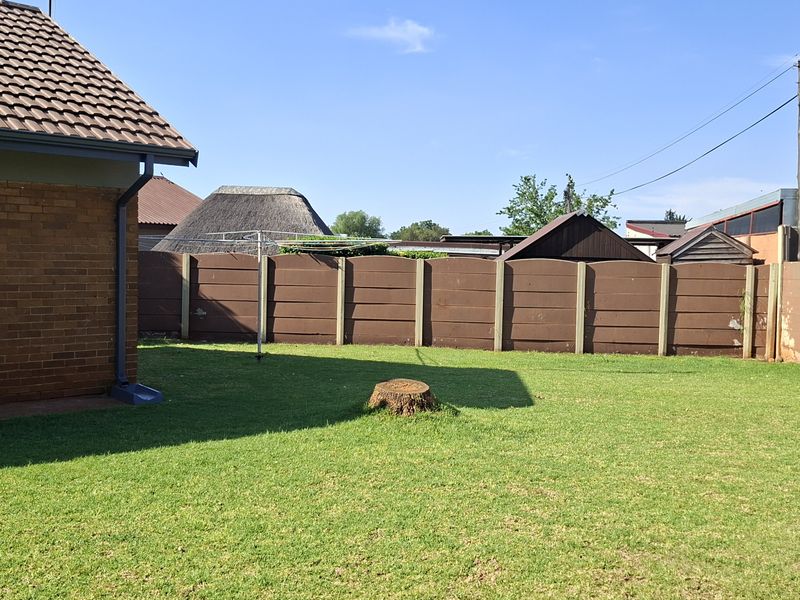 A spacious rear garden featuring a well-maintained lawn, enclosed by precast concrete boundary walls and adjacent to the brick-built house structure.