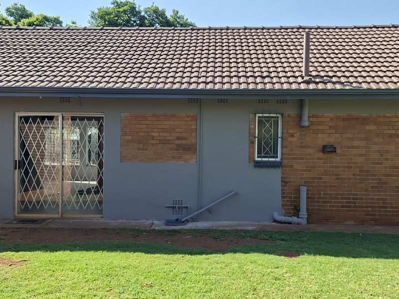 Rear exterior view of the house featuring a tiled roof, brick and painted plaster walls, and a sliding door with security gate.
