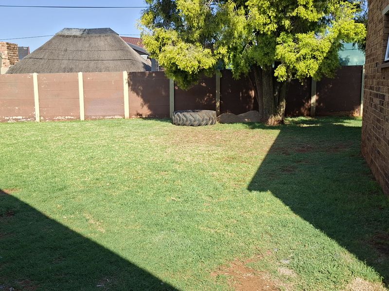A view of the rear garden featuring a lawn area, mature tree, and perimeter precast concrete walling adjacent to the brick house structure.