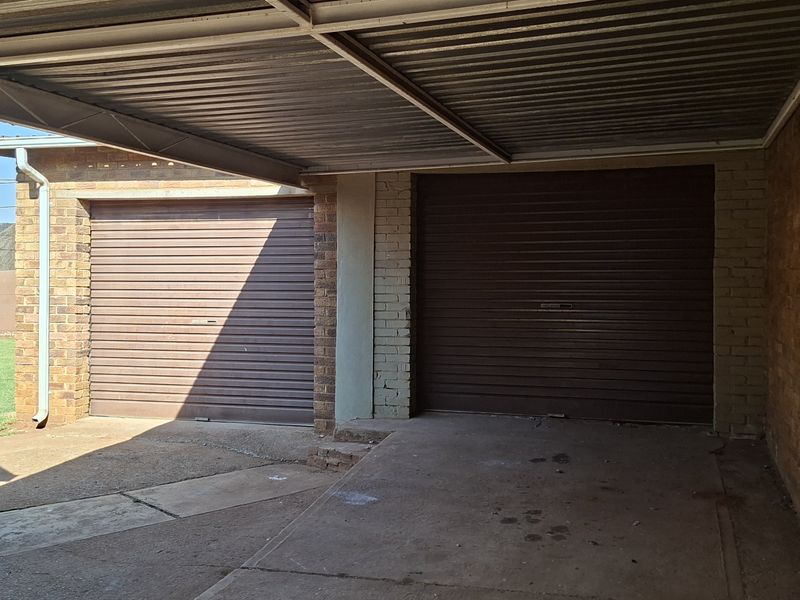 A functional double garage featuring roller doors and an attached covered carport area, set against a brick exterior with adjacent garden space.