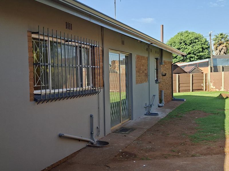 Rear exterior view of the house featuring a sliding glass door, security bars on windows, and a private backyard with a boundary wall.