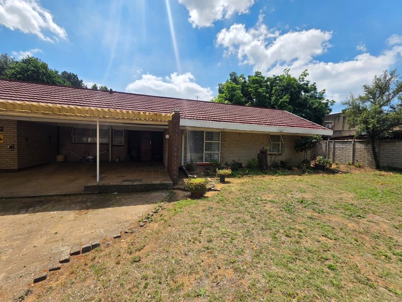 Front view of a single-story brick house featuring a tiled roof, an attached carport, and a paved driveway area.