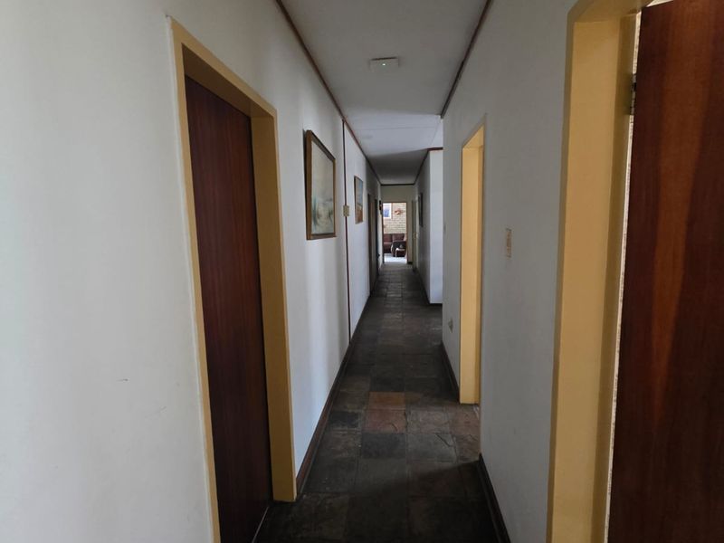 A long interior hallway featuring dark stone tile flooring and traditional wooden door frames, providing access to multiple rooms within the home.