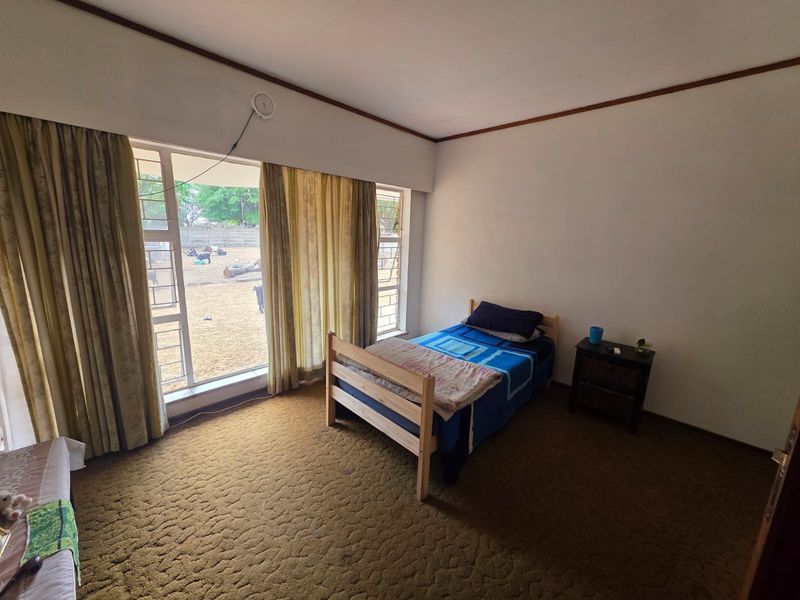 A bedroom featuring large windows with natural light, carpeted flooring, and neutral wall finishes, offering a blank canvas for potential updates.