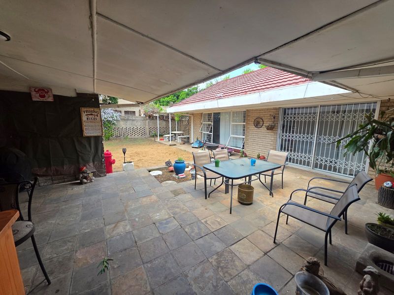 A covered outdoor patio area featuring stone paving, direct access to the home via sliding doors with security gates, and a view of the garden.