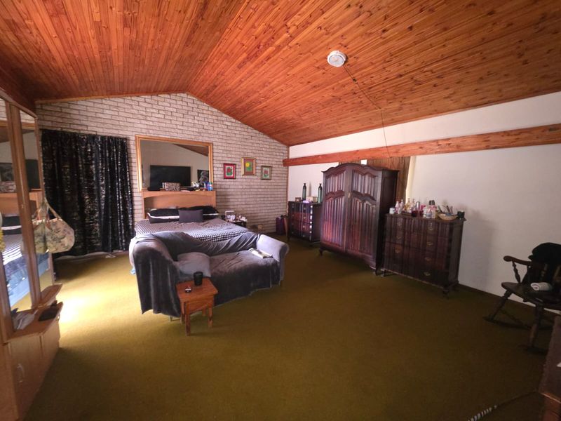 Spacious bedroom featuring a high raked timber ceiling, exposed brick wall, and carpeted flooring, offering a unique architectural character ready for modernization.