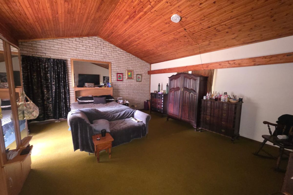Spacious bedroom featuring a high raked timber ceiling, exposed brick wall, and carpeted flooring, offering a unique architectural character ready for modernization.