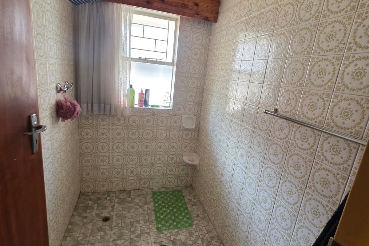 A dated shower enclosure featuring patterned wall and floor tiles, a fixed shower head, and a raised shower curb.
