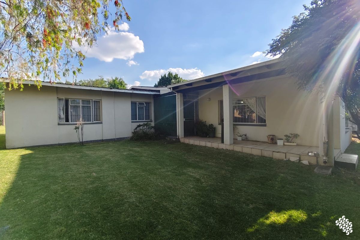 Rear view of the house featuring a covered tiled patio, metal window frames, and a well-maintained lawn area.