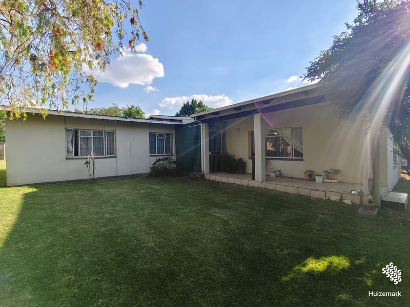 Rear view of the house featuring a covered tiled patio, metal window frames, and a well-maintained lawn area.